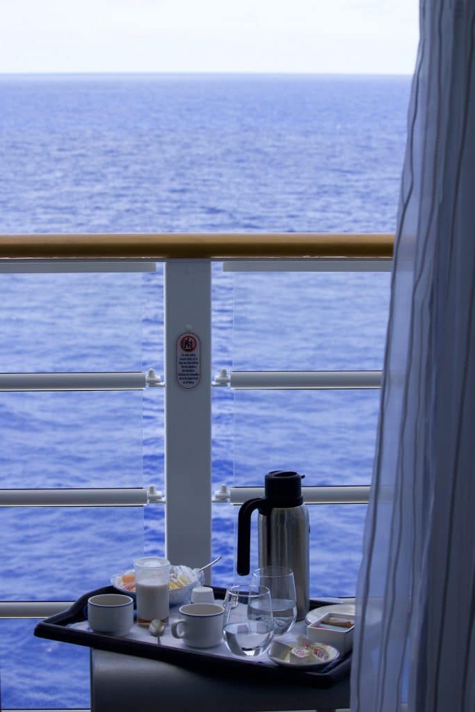 A room service tray filled with coffee, fruit, and water glasses on a verandah table on a Disney cruise. 