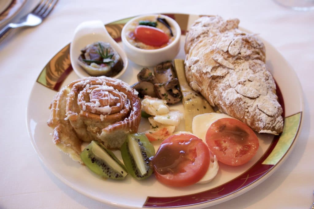 A plate filled with a croissant, sticky bun, kiwi, artichokes, and mozzarella cheese from Palo Brunch. 