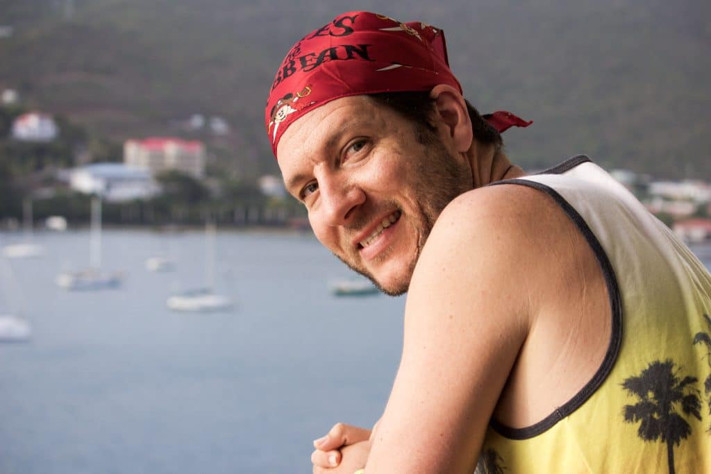 A man wearing a disney cruise pirate night bandana leaning over a railing by the water. 