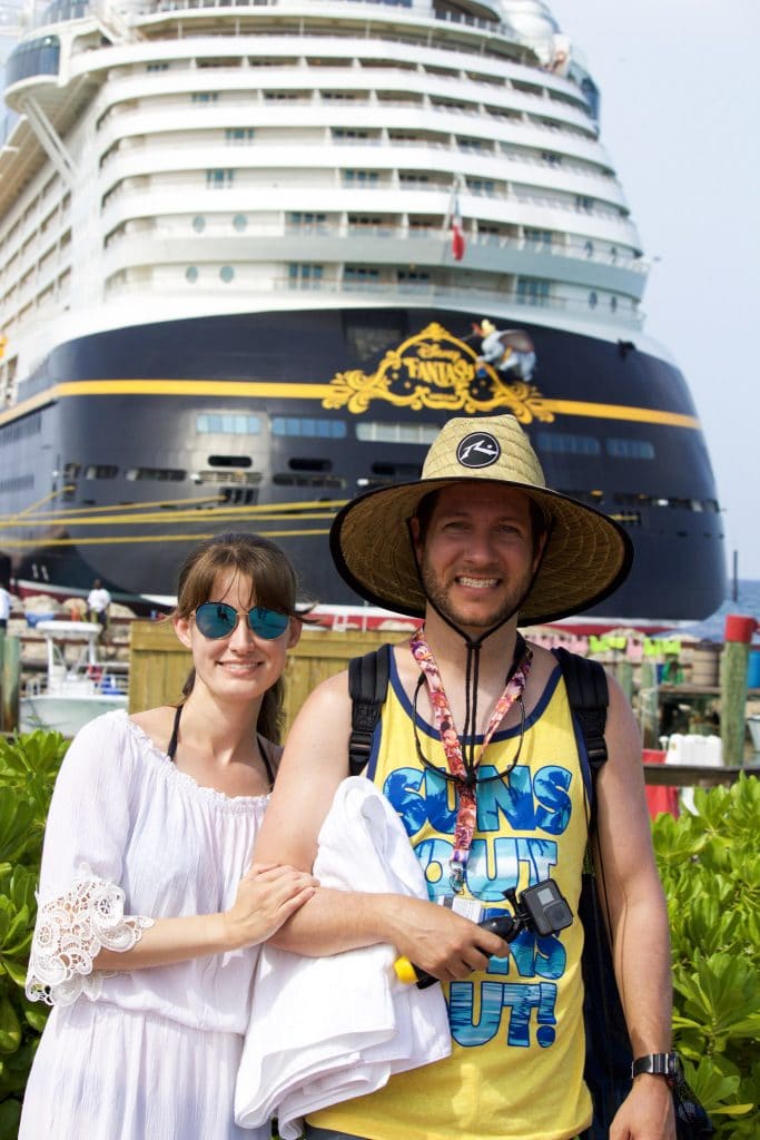 A happy couple standing in front of the Disney Fantasy ship on Castaway Cay. 