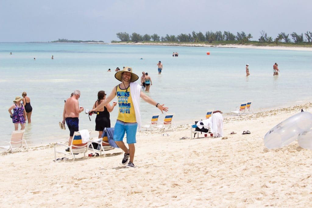 A man in a yellow tank top walking on the Serenity Bay beach at Castaway Cay.