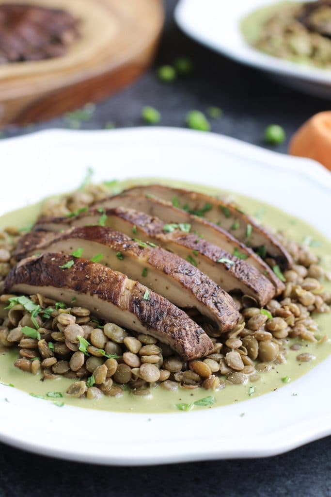 A sliced baked portobello mushroom on top of lentils and green sauce on a white plate. 