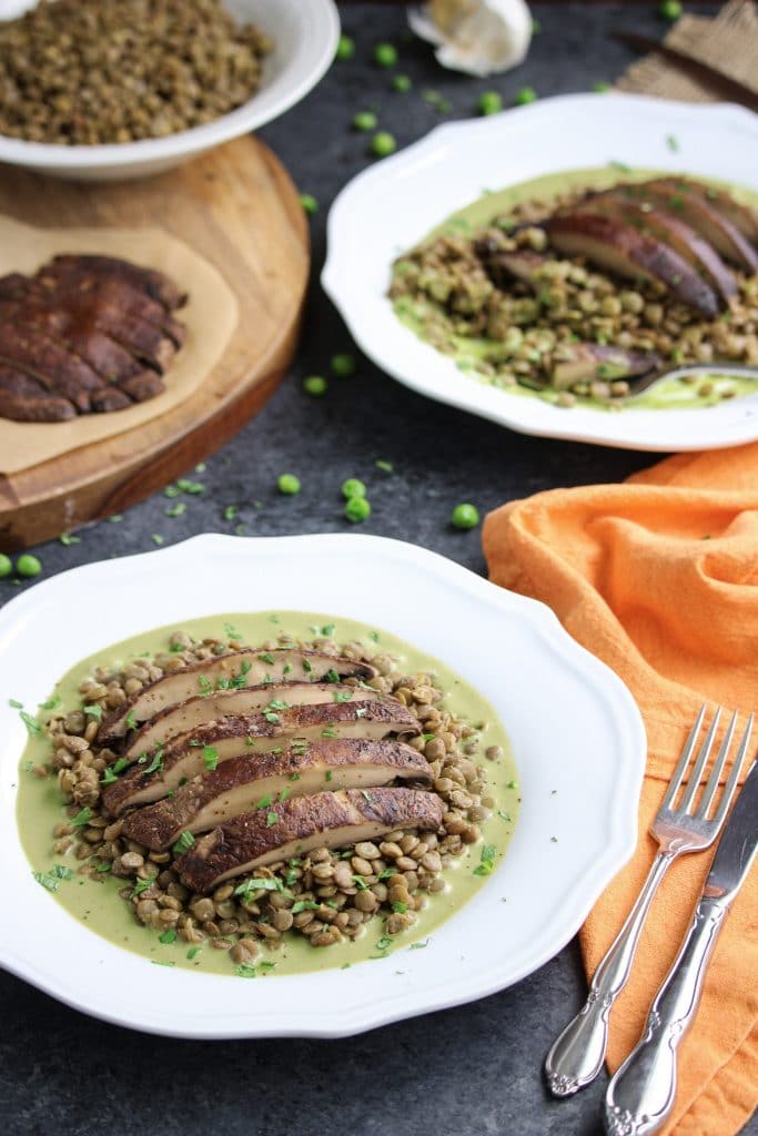 Two white plates filled with roasted portobello mushrooms on tp of green pea pesto lentils next to an orange napkin.