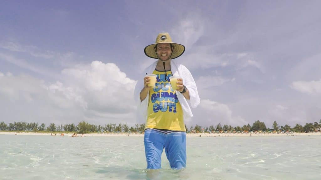 A man holding drinks while wading in shallow water in Serenity Bay at Castaway Cay.