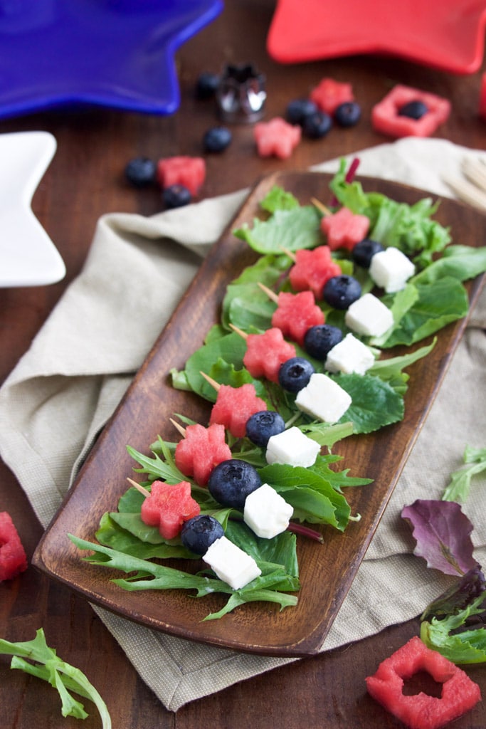 A platter of small skewers on a wooden platter on a rustic background.