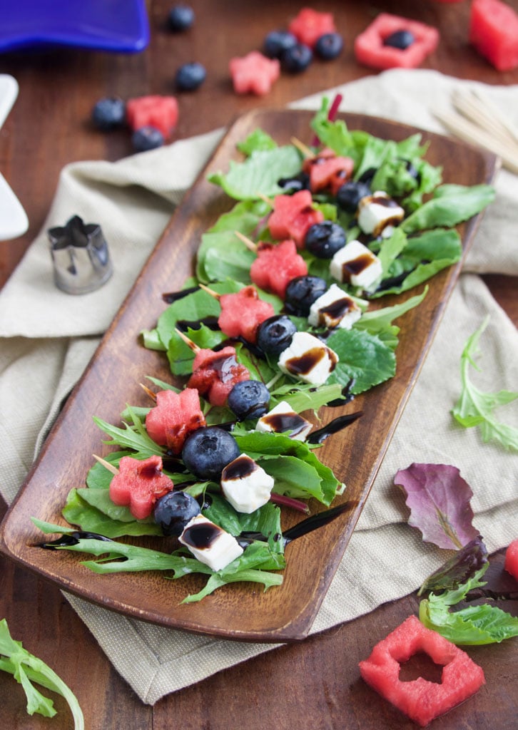 A platter of a red, white, and blue skewers on a wooden platter on top of a rustic background. 