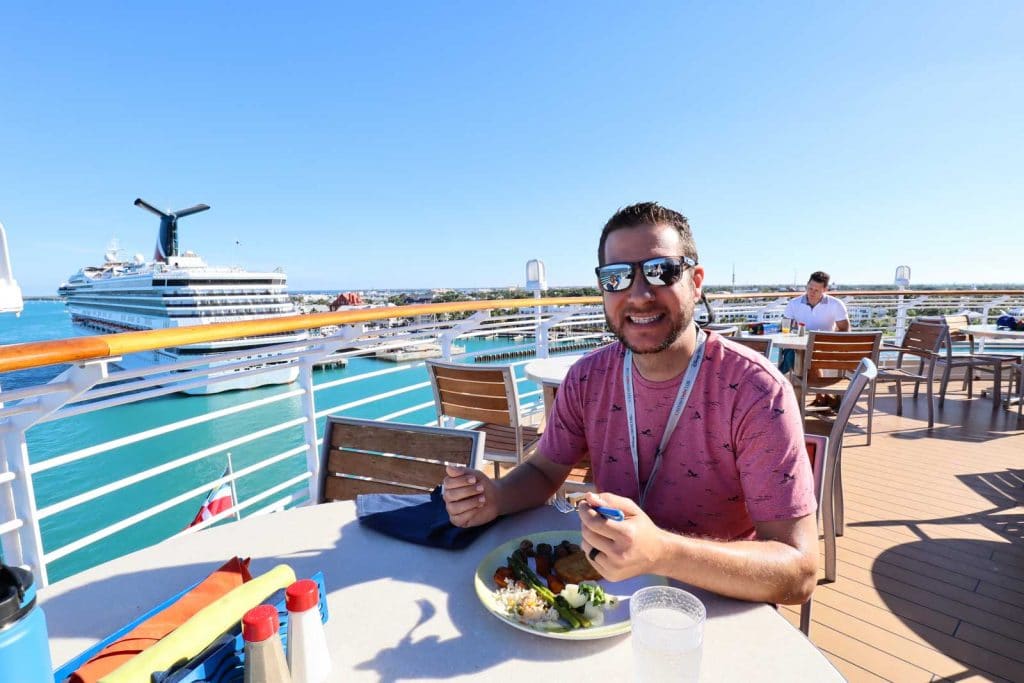 A man in a pink shirt is eating breakfast on the outside deck on the Disney Magic. 