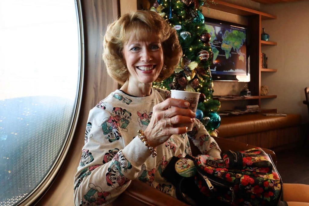 A woman holding a cup of coffee next t a christmas tree at Cove Cafe on the Disney Magic.