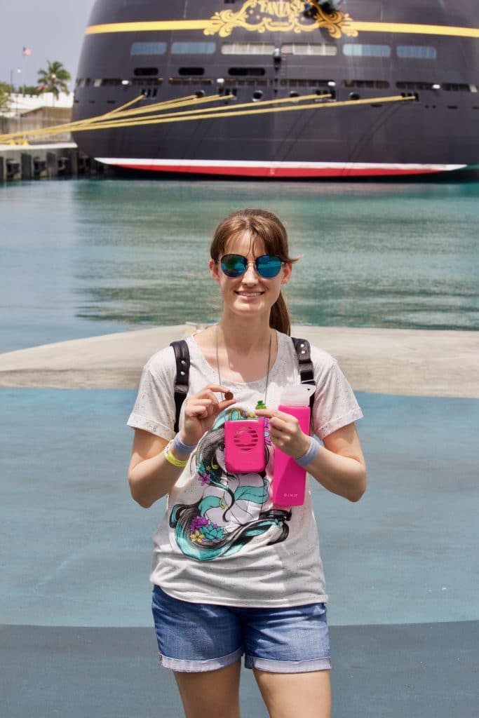 A woman is standing in front of the Disney Fantasy holding a pink water bottle and fan.