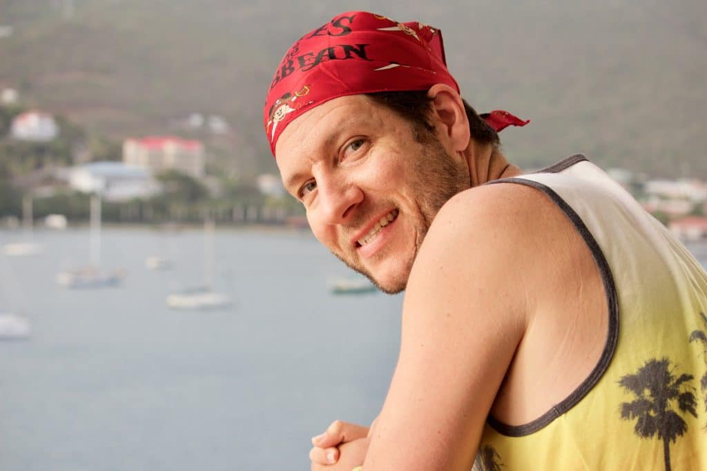 A man smiling and wearing a red Mickey pirate bandana while leaning over a railing on a Disney cruise.
