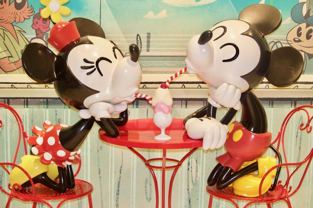 Mickey and Minnie sharing ice cream at a red table at Sweet on You on Disney Fantasy.