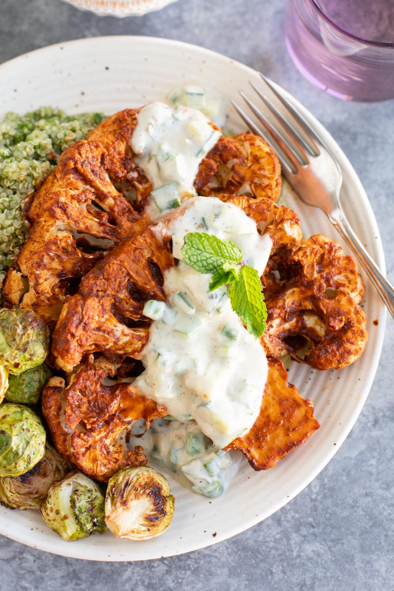 A close up view of roasted cauliflower steaks topped with sauce on a plate. 