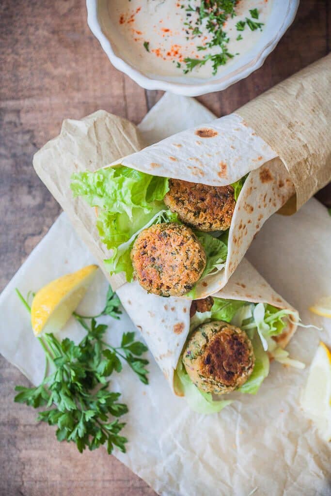 Two vegan falafel wraps on a piece of parchment paper on a rustic background. 