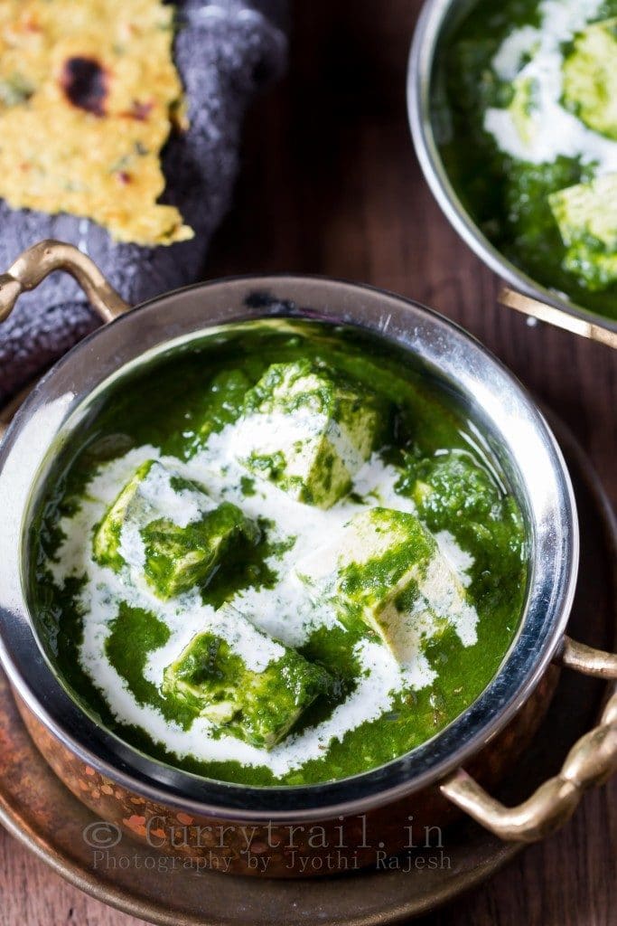 Two bowls filled with tofu in green spinach sauce on a rustic background.