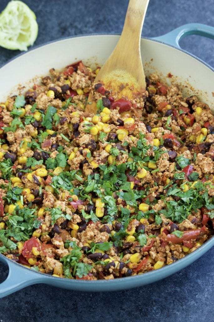 A large blue pan filled with vegetables and a wooden spoon on a dark background. 