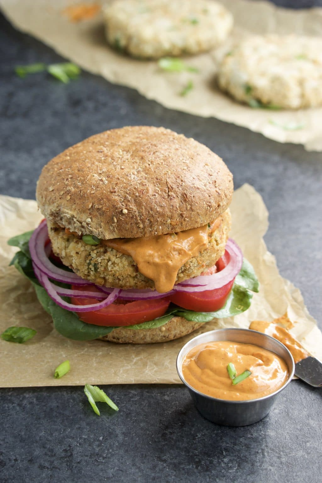 A veggie burger on top of piece of parchment paper next to a small bowl of chipotle sauce. 