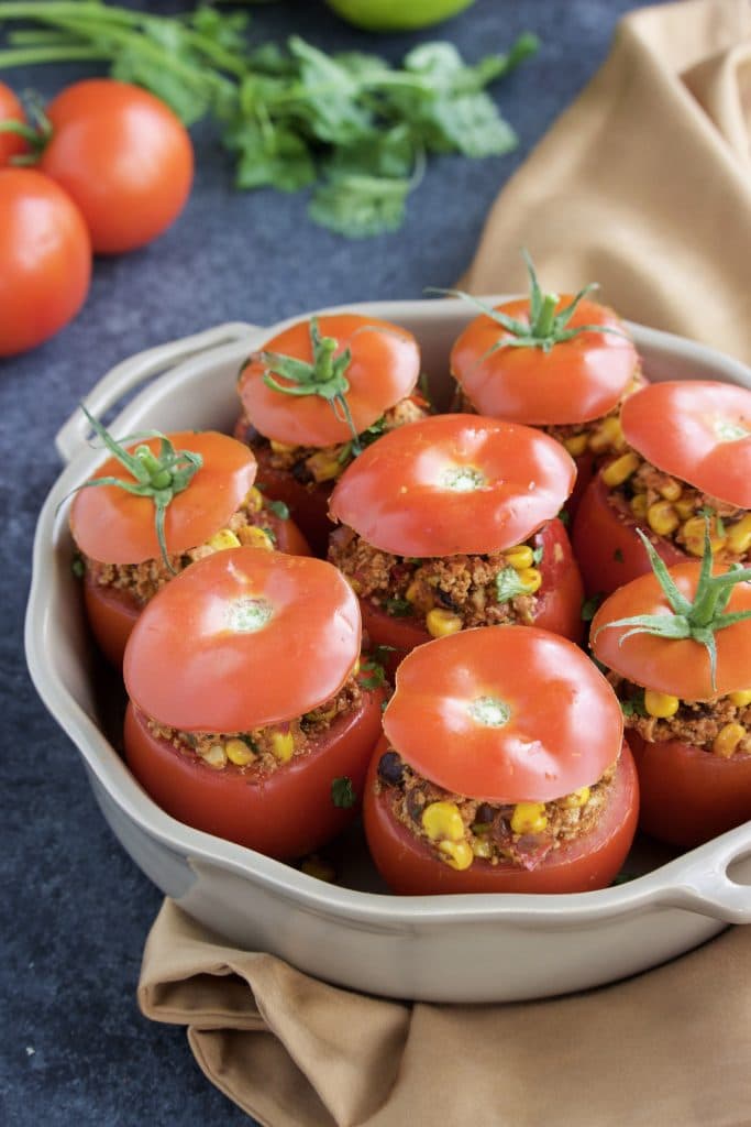 A casserole dish filled with stuffed tomatoes with the tops put back on. 