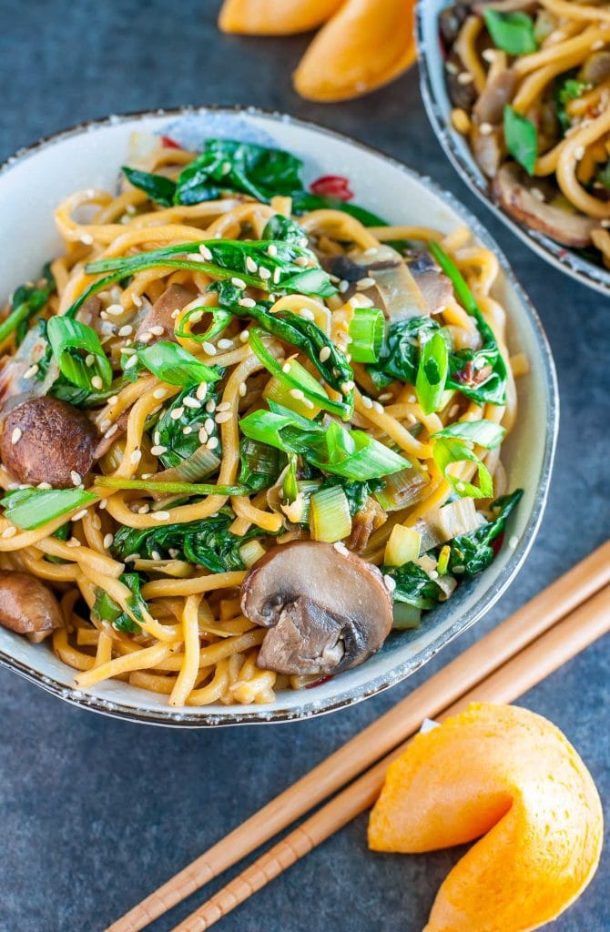 Two bowls filled with noodles mushrooms and spinach on a dark background.