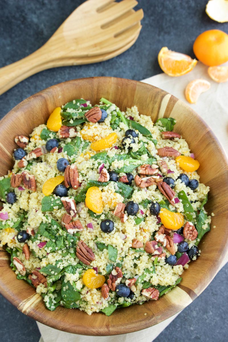A large wooden bowl filled with salad on a dark gray background. 