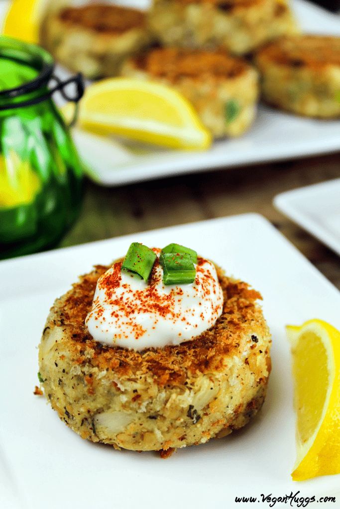 A vegan crab cake topped with sauce and green onions on a square white plate.