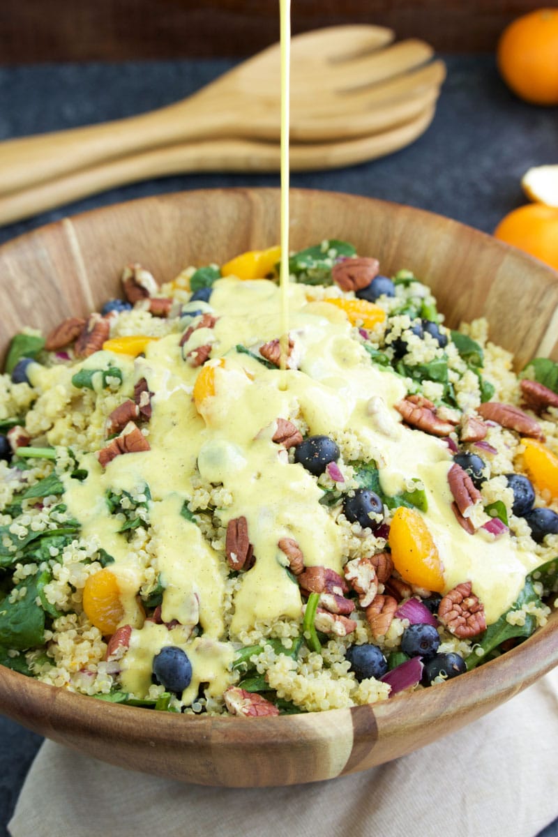 Dressing being poured over salad in a large wooden bowl on a dark gray background.