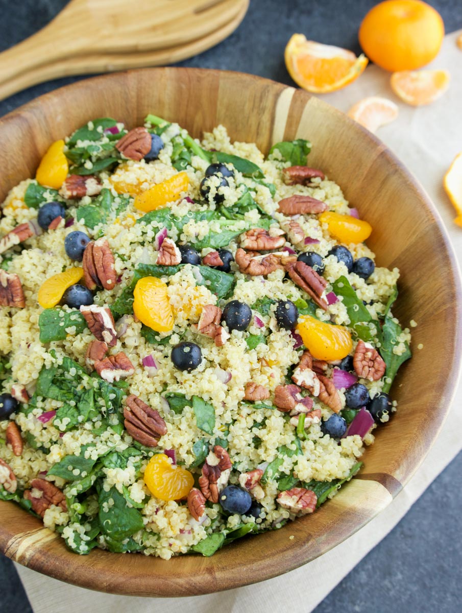 A large wooden bowl filled with mango quinoa salad on a dark background. 