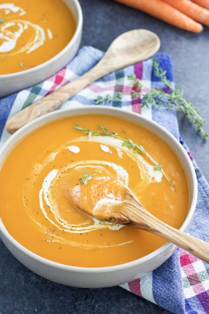 A bowl filled with soup and a wooden spoon next to a plaid napkin. 