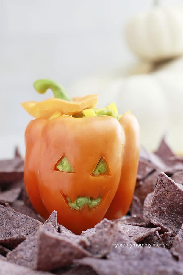 An orange bell pepper filled with guacamole on top of purple tortilla chips. 