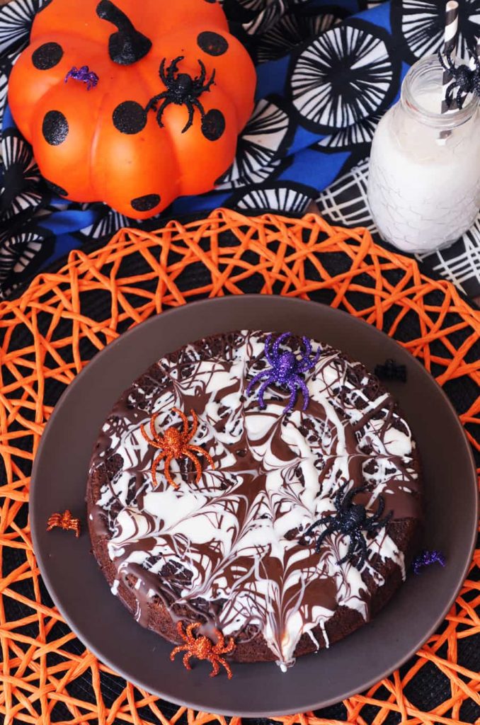 A vegan chocolate cake with a frosting spider wed and fake spiders on a colorful background. 