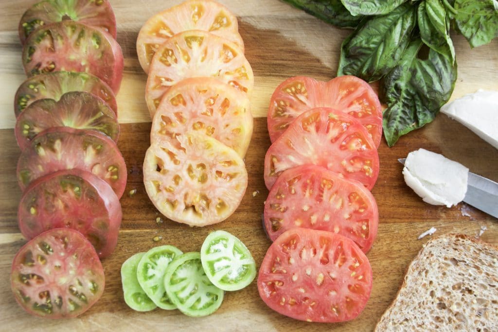 Multiple slices of heirloom tomatoes and basil on a cutting board.