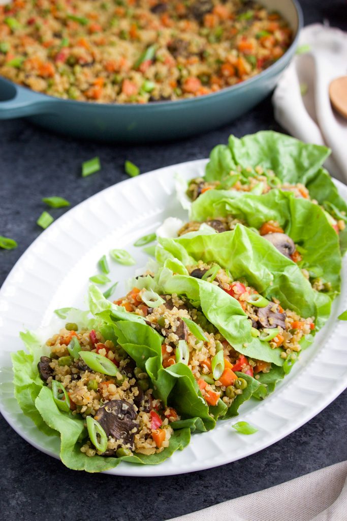 Lettuce wraps filled with quinoa and vegetables on a large white platter next to full pan.