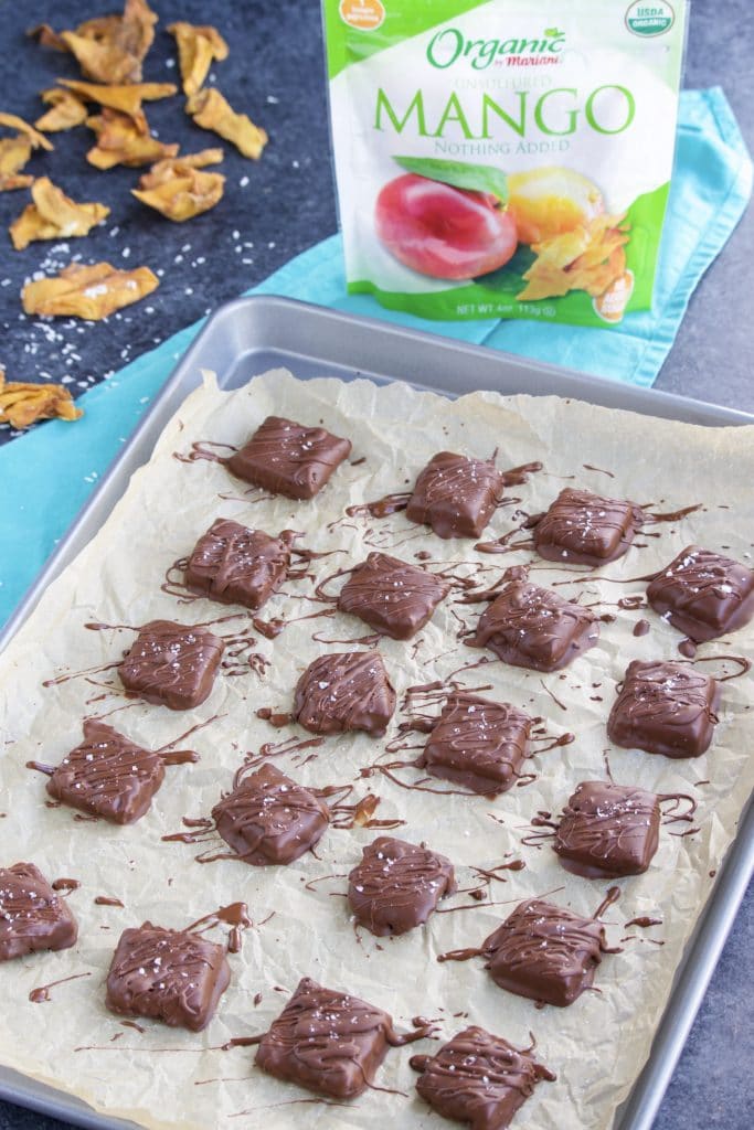 A tray of chocolate candy on a parchment lined tray next to a bag of organic dried mango.