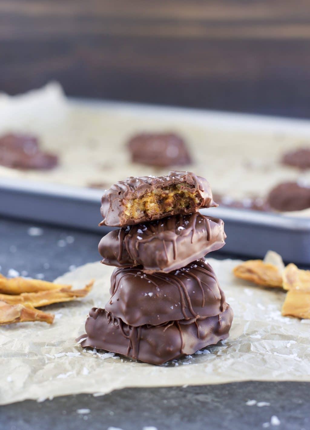 een stapel van vier vegan chocolade snoepjes op een stuk perkamentpapier naast een bakplaat. 