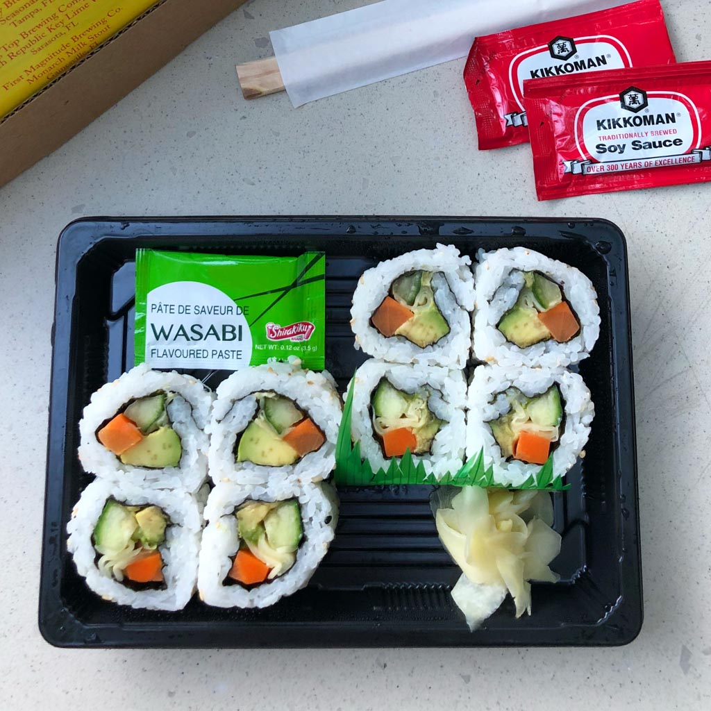 Vegetable sushi on a black tray sitting on a table. 