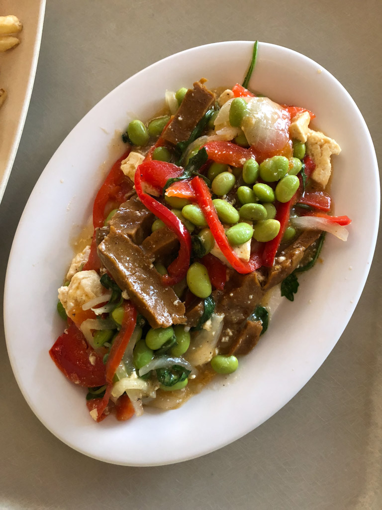 A vegan seitan scramble with vegetables on a white plate from the Art of Animation food court in Disney World. 