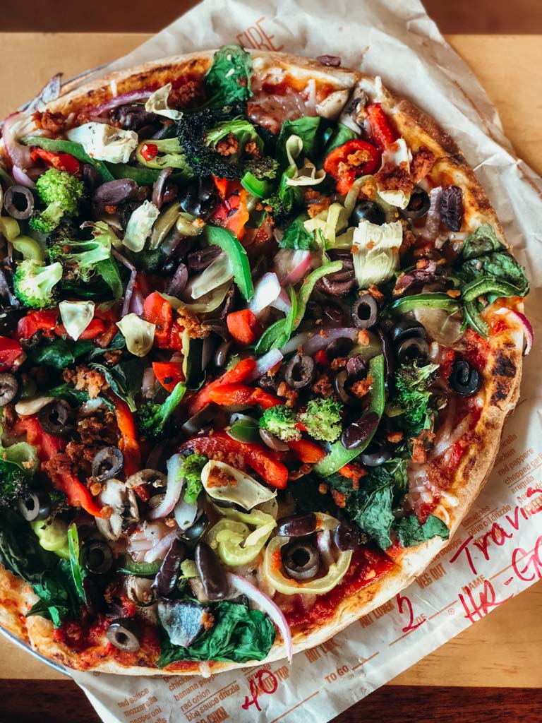 Vegan Blaze pizza loaded with vegetables on a parchment paper lined tray that's sitting on top of a table. 
