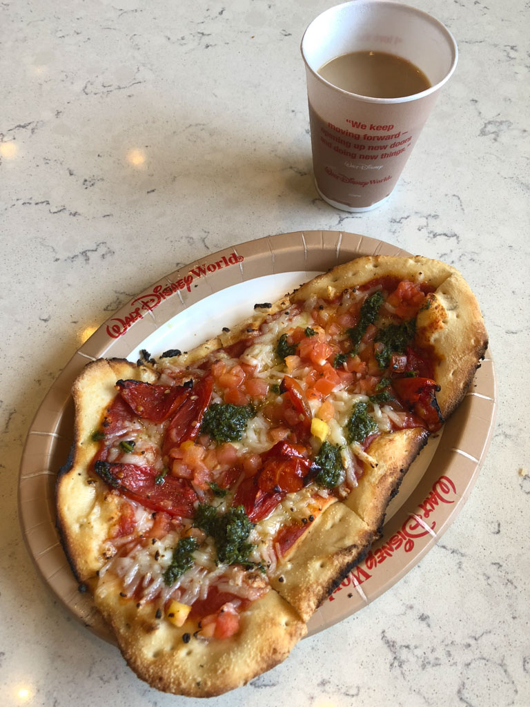 A cup of coffee and vegan flatbread pizza on a paper plate from Gasparilla Island Grill at the Grand Floridian Resort in Disney World. 