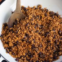 A large white pan filled with vegan taco meat being stirred by a wooden spoon.