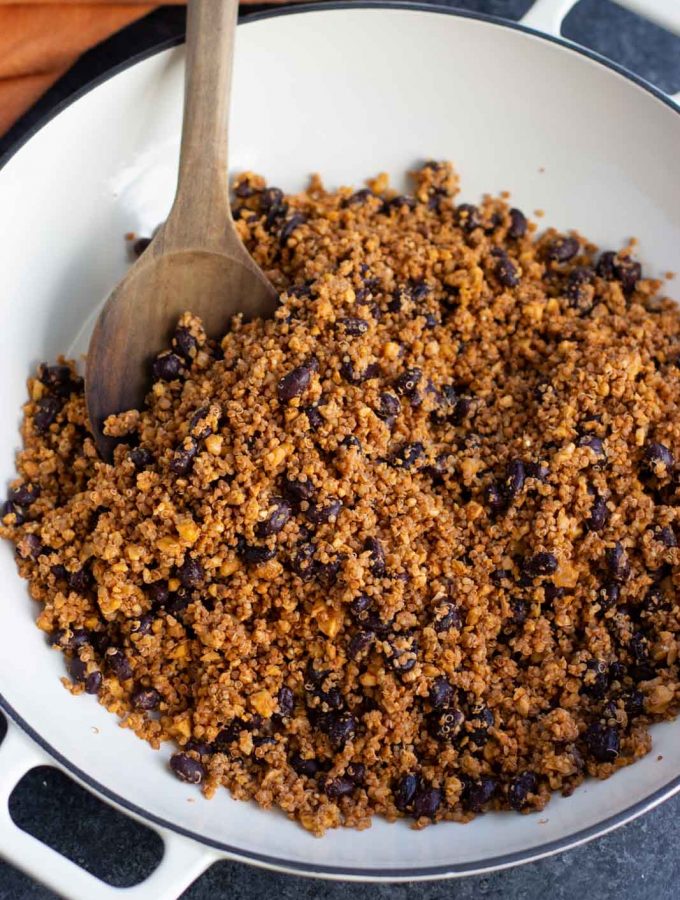 A large white pan filled with vegan taco meat being stirred by a wooden spoon.