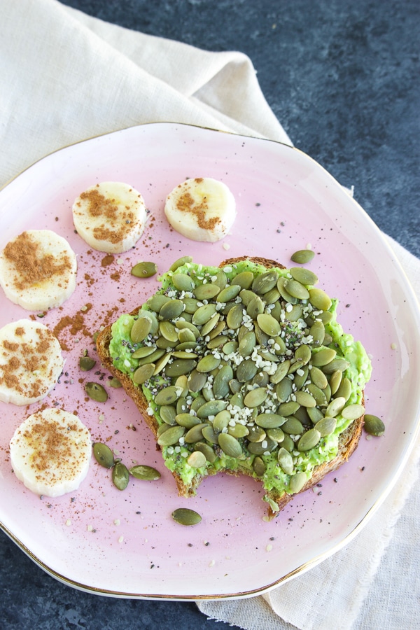 A pink plate with toast and banana coins on it next to a beige napkin on a dark background.