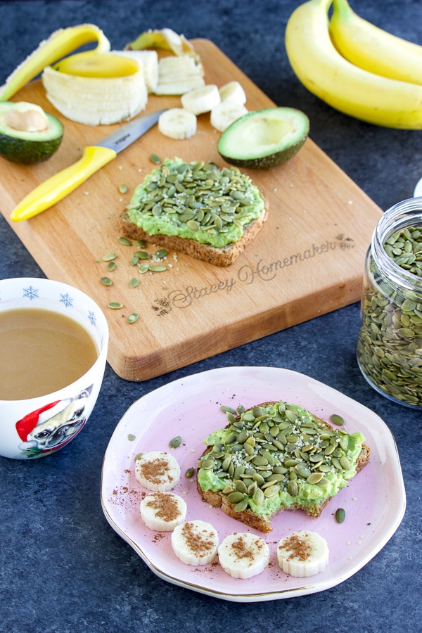 A pink plate with toast and banana coins on it next to a coffee cup and cutting board with food on it.