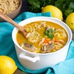 Soup in a white bowl on top of an aqua napkin next to a few lemons.