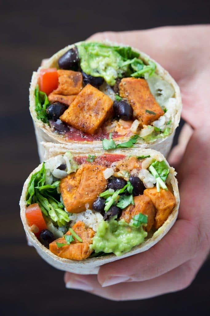 A hand holding a vegan burrito cut in half and stacked on top of each other.