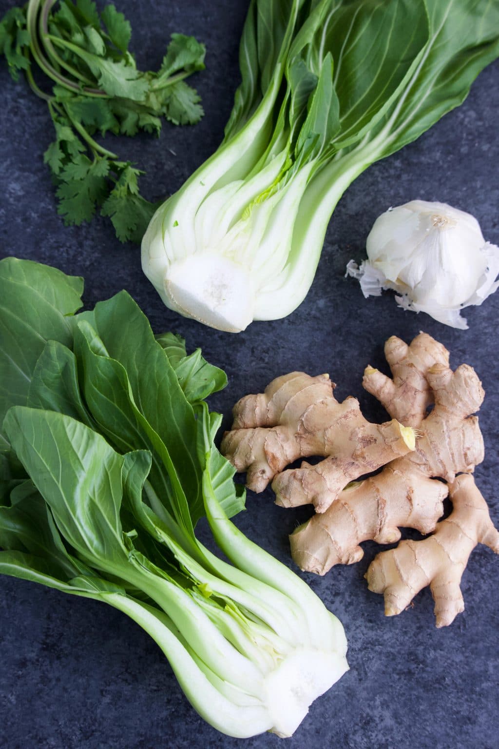 Bok choy, ginger, garlic, and cilantro laying on a dark background.