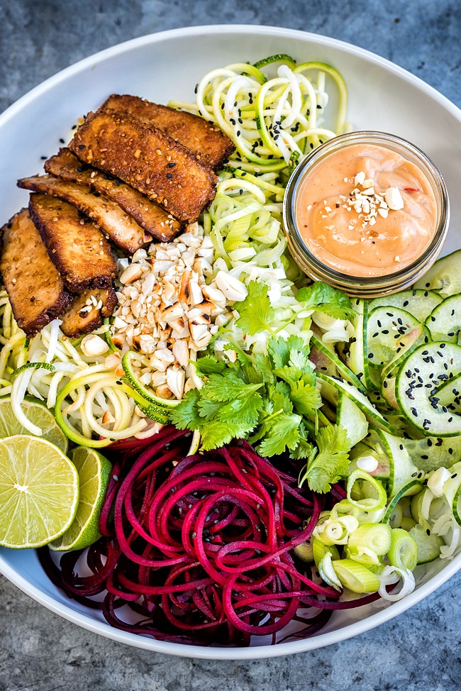 A low-carb vegan bowl of spiraled zucchini noodles with spicy tofu and peanut sauce on a textured background. 