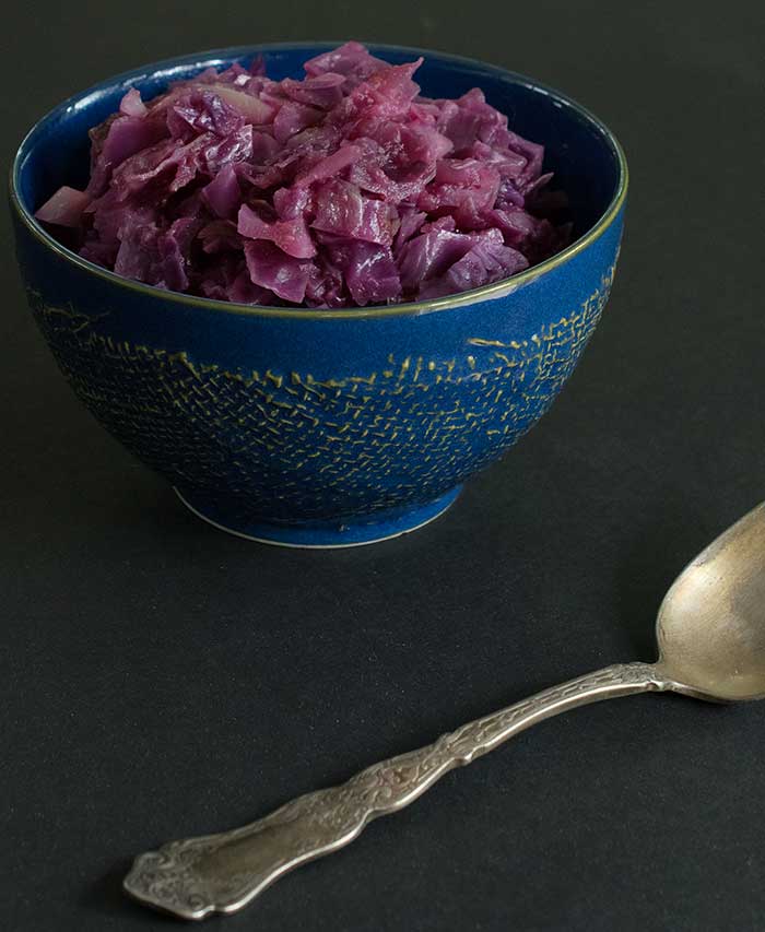 A small blue bowl of loq-carb vegan sweet and sour red cabbage on a black background.
