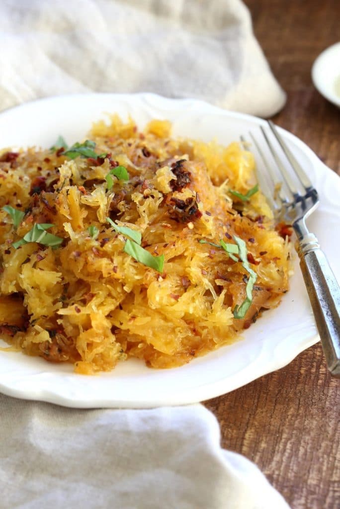 Low-carb vegan spaghetti squash pasta topped with basil in a white bowl on a rustic background.