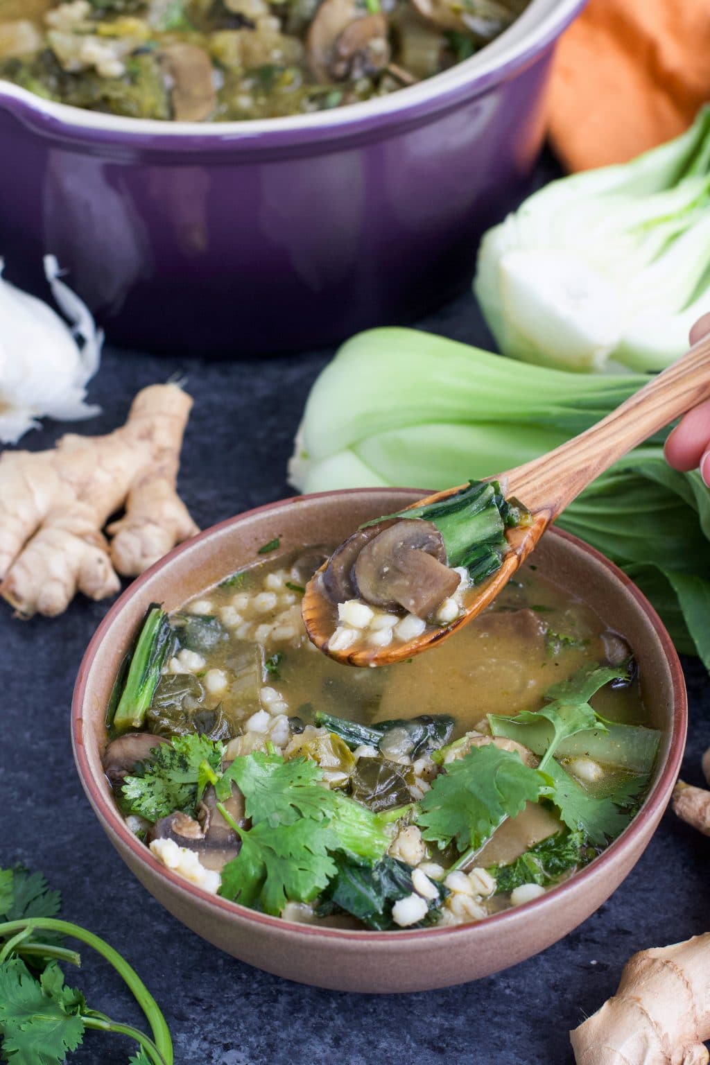 A brown bowl filled with bok choy soup and a spoon dipping into the bowl.