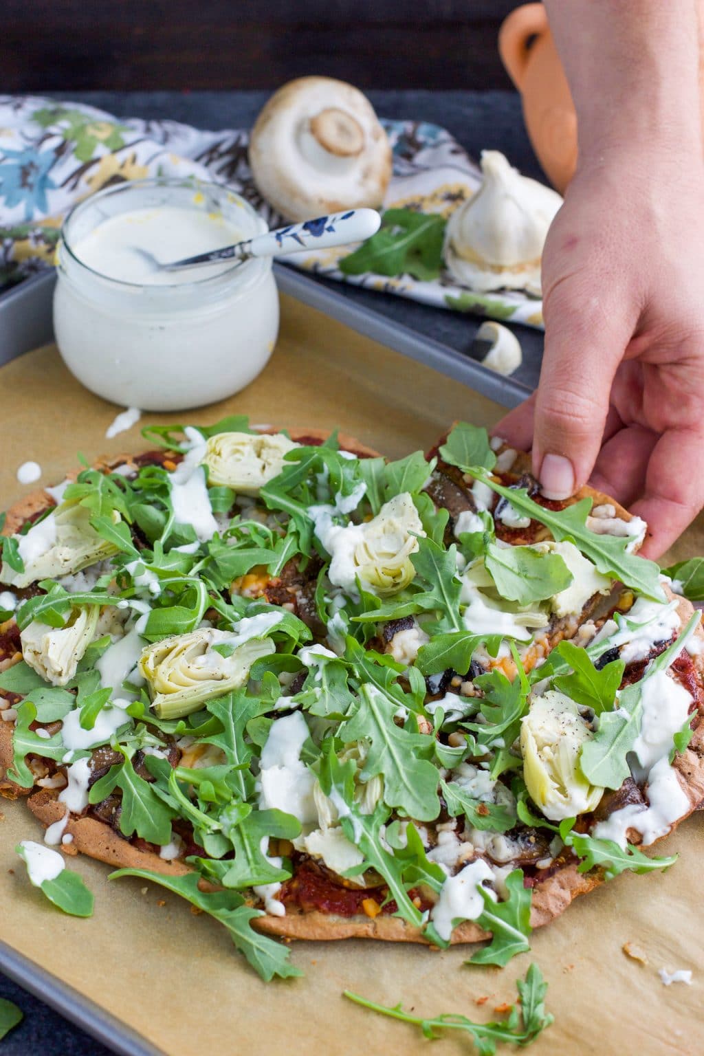 A hand grabbing a piece of pizza from a parchment paper lined tray.
