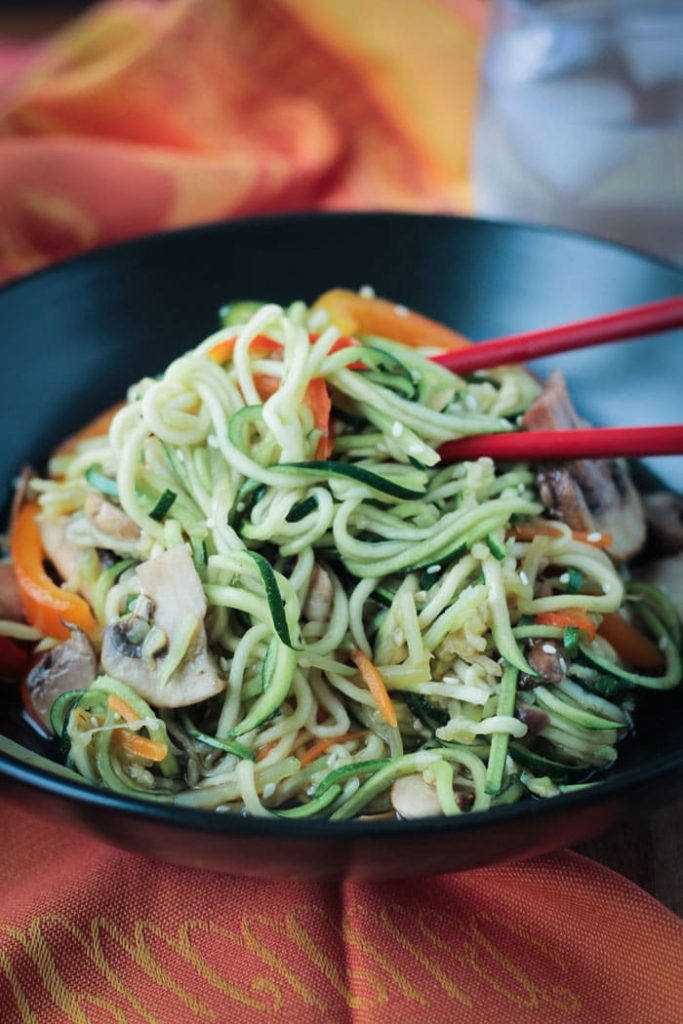 Low-carb vegan stir fry zucchini noodles with vegetables and chopsticks on the side of a large black bowl.